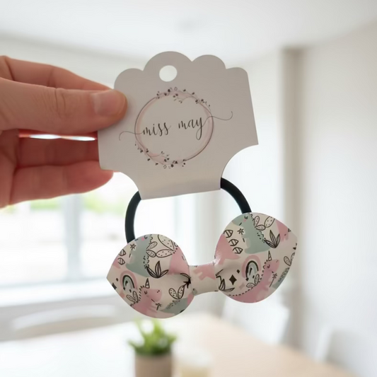 Hair ties with decorative bows held by a hand against a blurred indoor background
